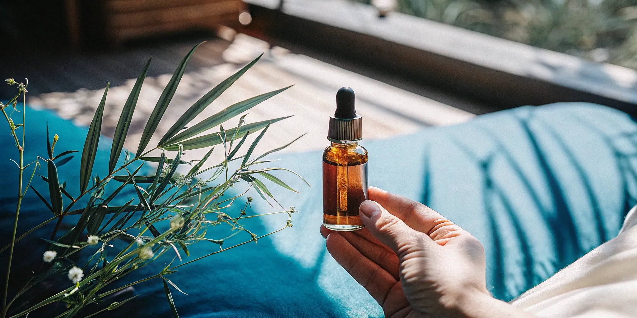 A hand holds a dropper bottle of organic full spectrum CBD tincture next to hemp leaves.